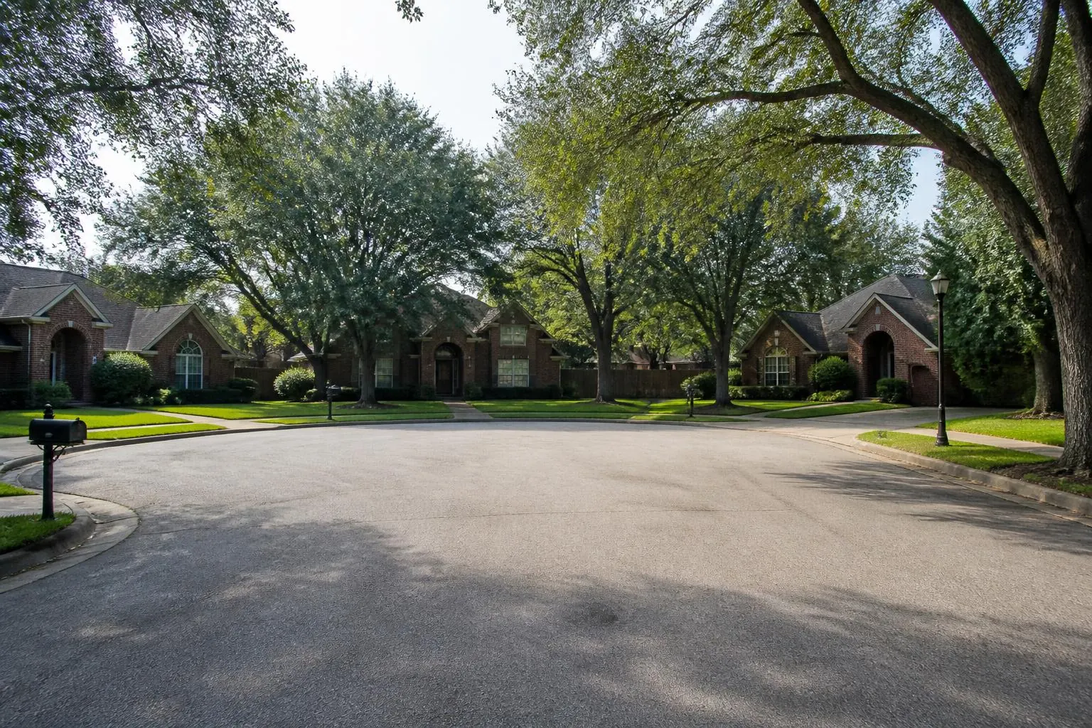 A shaded suburban cul-de-sac ringed by brick homes and mature oaks in morning light