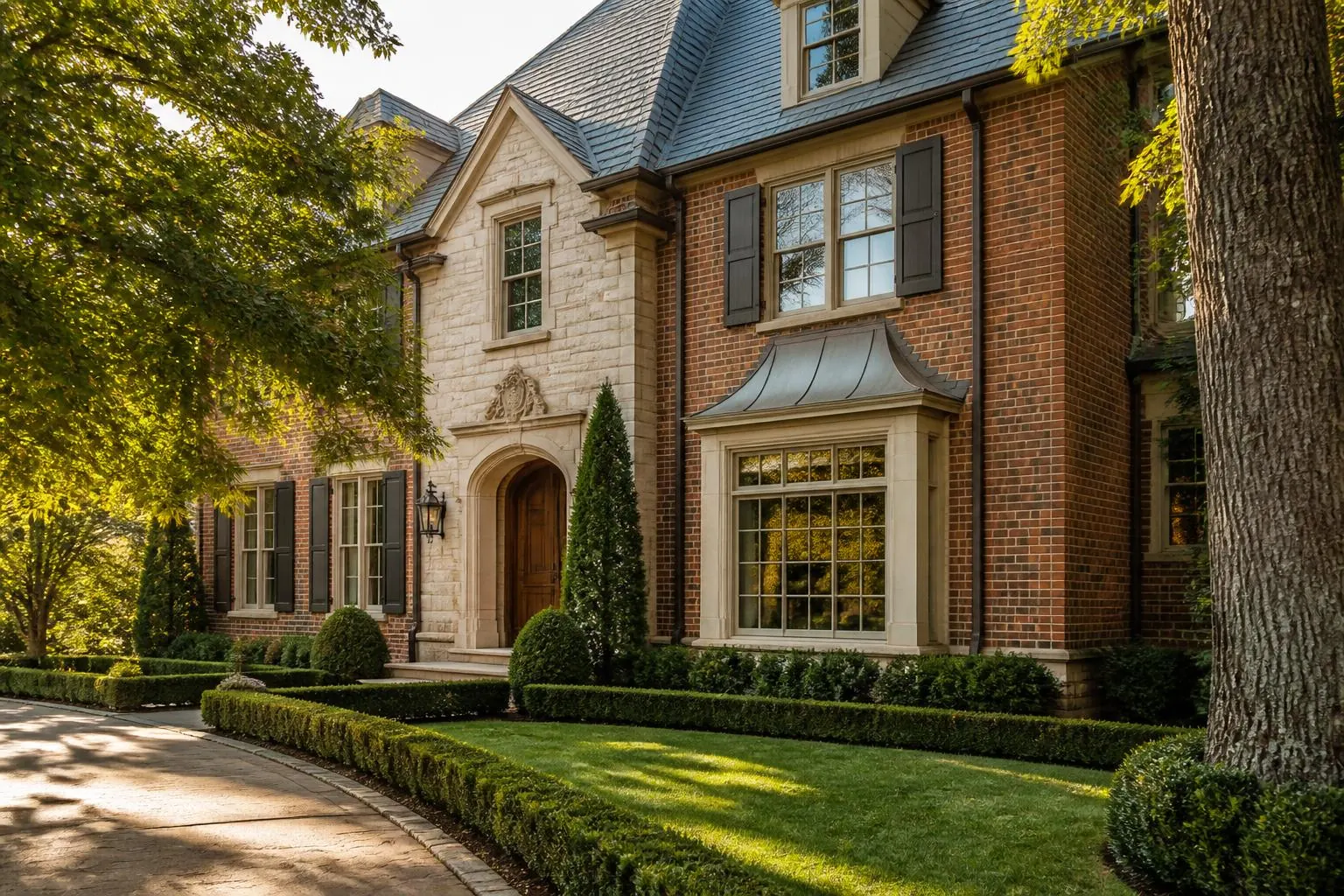 A brick and limestone two-story Charlotte home with slate roof, boxwood hedges and a curved drive
