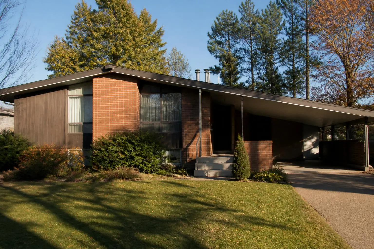 A 1960s split-level house with brick and vertical wood siding and an attached carport
